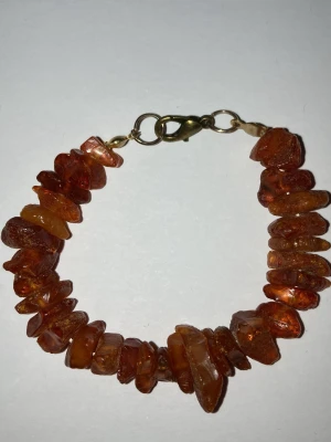 Armband med bärnstensfärgade plast stenar - Handgjort armband av mig som är coolt med oregelbundna bärnstensfärgade plast stenar och guldfärgat spänne. Stenarna har en naturlig, rå känsla och ger ett unikt uttryck. Perfekt accessoar för dig som gillar boho-stil och jordnära toner. Frakten är 22-100kr beroende på vikt. Kontakta mig om du har frågor eller vill köpa.