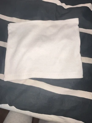 Vit bandeau tubtopp - Säljer en enkel och stilren vit bandeau tubtopp. Toppen är ärmlös och har en mjuk, stretchig känsla som sitter skönt på kroppen. Perfekt att matcha med höga jeans eller kjol för en clean look.