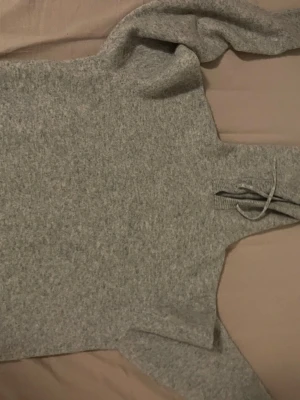 Ljusgrå stickad polotröja - Mysig ljusgrå stickad polotröja med långa ärmar och hög krage. Tröjan har en relaxed fit och är tillverkad i ett mjukt material som känns skönt mot huden. Perfekt för kyliga dagar och enkel att matcha med olika outfits.