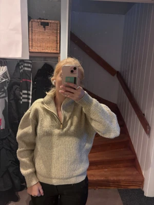 Beige stickad tröja med dragkedja - Mysig beige stickad tröja med halv dragkedja och hög krage. Tröjan har en avslappnad passform, ribbstickade muddar och är tillverkad i ett grovt stickat material. Perfekt för kalla dagar och enkel att matcha med olika outfits.