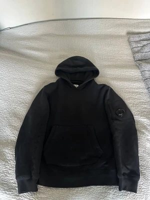 Svart hoodie från C.P. Company - Säljer denna hoodie från C.P. Company! Köpt på NK för 1899kr. Bra skick, inga hål eller slitningar. Storlek: 140cm men passar upp till 155cm ungefär. Ställ gärna frågor!