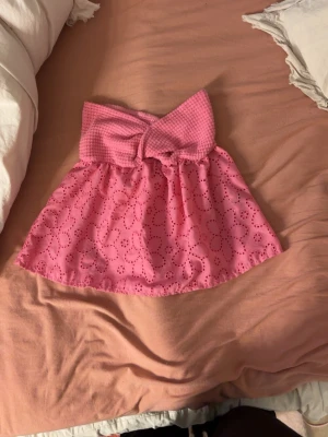 Rosa bandeau tubtopp - Rosa bandeau tubtopp med twistad överdel i ribbat tyg och broderade blommor på den luftiga nederdelen. Toppen är axelbandslös och har en söt, feminin look som passar perfekt till sommaren.