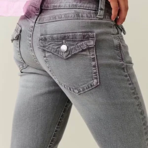 Grå bootcut jeans med fickdetaljer - Säljer ett par grå jeans med bootcut passform och snygga ficklock med knapp bak. Jeansen har en klassisk femficksdesign och är gjorda i stretchigt denim som sitter riktigt bra. 