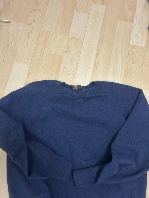 Mörkblå stickad tröja Oscar Jacobson - Mörkblå stickad tröja från Oscar Jacobson, tillverkad i Italien. Tröjan har rund halsringning och ribbstickade muddar vid ärmslut och nederkant. Perfekt för dig som gillar klassisk och stilren design.