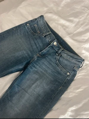 Blå flare jeans i klassisk modell - Säljer ett par blå bootcut jeans med fem fickor och låg midja. Jeansen har en klassisk tvätt och raka ben som blir vidare nedtill. Perfekta till sneakers eller boots och formar kroppen jätte fint .