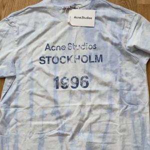 Acne Studios blåvit t-shirt - Säljer en snygg blåvit t-shirt från Acne Studios med tryck 'STOCKHOLM 1996' framtill. T-shirten har korta ärmar, rund hals och är gjord i mjuk bomull. Perfekt för dig som gillar stilrena plagg med en twist. Både till men och tjejer 