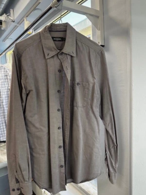 Grå skjorta från Dressmann slim fit - Säljer en stilren grå skjorta från Dressmann i slim fit-modell. Skjortan är tillverkad i 100% bomull, har långa ärmar, klassisk krage och bröstficka med knapp. Perfekt till jeans eller chinos för en clean look.