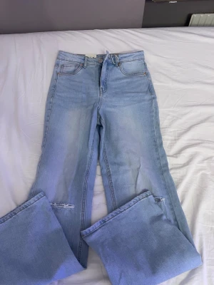 Ljusblå wide jeans från LAB Industries - Säljer ett par ljusblå jeans från LAB Industries med breda ben och slitningar vid knäna. Jeansen har klassisk femficksdesign, hög midja och är tillverkade i mjuk bomullsdenim. Perfekta för en avslappnad och trendig look.