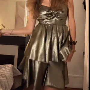 Balklänning/cocktail klänning - Säljer en glansig guldig klänning med volanger och omlott. Så himla snygg. Helt oanvänd och köpt för ca 2000kr
