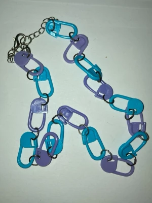 Lila och turkost plastlänkhalsband - Handgjort färgglatt halsband med stora länkar i plast i lila och turkost. Länkarna är ovala och sitter ihop med metallringar. Halsbandet har ett justerbart kedjelås i metall. Perfekt för dig som gillar statement-smycken och vill sticka ut. Frakt 22-100kr. Kontakta mig om du vill köpa eller har frågor.