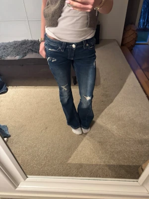 Blå bootcut jeans med slitningar - Snygga blå bootcut jeans med slitna detaljer på knän och lår. Låg midja och vita sömmar. Använda ett fåtal gånger