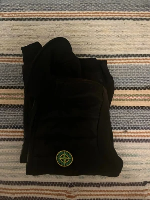 Svart duncardigan - Snygg svart dunväst från Stone Island med klassisk logotyp på bröstet. Västen har dragkedja framtill och praktiska fickor med dragkedja. Perfekt för lager-på-lager och streetwear-stil. Materialet är lätt och isolerande för extra värme. Det står i jackan att det är L men den passar på M