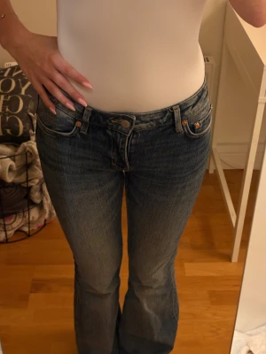 blå bootcut jeans - Säljer ett par klassiska jeans i blå tvätt med bootcut passform. Jeansen har låg midja, fem fickor och snygga kontrastsömmar. Tillverkade i slitstarkt jeanstyg med en lätt tvättad look. Perfekta för dig som gillar retrovibbar och tidlös stil.