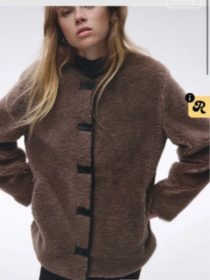 Brun teddyjacka med knappar - Mysig brun teddyjacka med svarta knappar framtill. Jackan har en rak passform och är tillverkad i ett fluffigt teddy-material som ger en cool och avslappnad look. Perfekt för att hålla värmen under kyliga dagar.