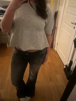 Grå croppad tröja med volang - Grå croppad tröja med volangkant och halvlånga ärmar. Tröjan har rund halsringning och är gjord i ett mjukt stickat material. Perfekt för en avslappnad och trendig look. Aldrig använd!