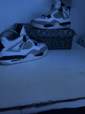 Nike Air Jordan 4 White/Black - Säljer ett par Nike Air Jordan 4 i vitt och svart med meshpaneler och grå mockadetaljer. Skorna har den klassiska Jumpman-loggan på plösen och sulan, samt snörning och en chunky sula med synlig Air-enhet. Box medföljer.pris inte hugget i sten