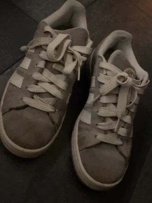 Grå adidas campus  - Säljer mina grå adidas campus i storlek 38, med vita streck. Har inte använt så mycket så är i bra skick men små tecken på användning.