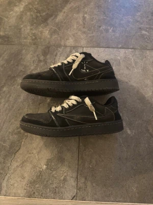 Svarta Nike Dunk sneakers med vita detaljer - Säljer ett par svarta Nike Dunk sneakers med vita kontrastsömmar och vita snören. Skorna har låg profil, perforerad tå och klassisk Nike-logga på plösen. Snygg streetstil som passar perfekt till jeans eller shorts.