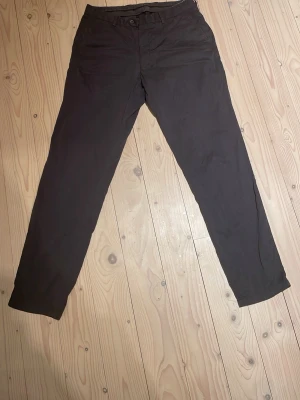 Mörkgråa chinos med rak passform - Snygga mörkgråa chinos med rak passform och klassisk design. Byxorna har knapp- och dragkedjegylf samt fickor som ger en clean look. Perfekta för dig som vill ha ett stilrent och enkelt plagg i garderoben. Materialet känns mjukt och bekvämt.                  Var inte rädd för att skriva om du har några frågor!