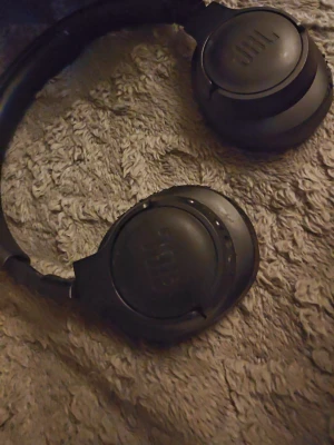 Svarta over-ear hörlurar från JBL - Snygga svarta over-ear hörlurar från JBL med rund form och vadderade kåpor. Tillverkade i plast och konstläder, med JBL-loggan på sidorna. Perfekta för musik, gaming eller film och har en stilren design som passar till det mesta. Ps lite slitna men annars funkar dom perfekt...