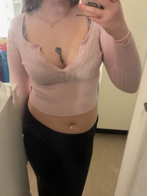 Ljusrosa ribbad croppad topp - Säljer en ljusrosa croppad topp med ribbad struktur och v-ringning med knappar. Toppen har långa ärmar och är i ett mjukt, stretchigt material som sitter snyggt på kroppen. 