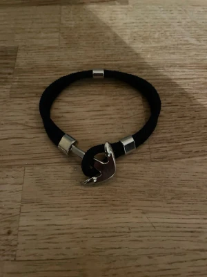 Marinblått armband med krokspänne - Snyggt marinblått armband i textil med silverfärgade metalldetaljer och ett unikt krokformat spänne. Perfekt accessoar för dig som gillar stilrena och moderna smycken med en twist.