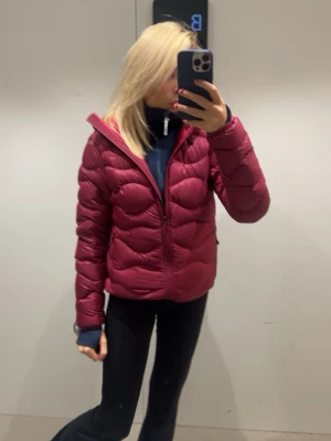 Mörkröd puffer dunjacka - Snygg mörkröd puffer dunjacka med quiltad design och dragkedja framtill. Jackan är andvänd ungefär 5 gånger och är sprillans ny i skicket. Säljer för att jag fick en i mörkblå i present och passar inte så bra i vinröd! Storlek xs - xxs