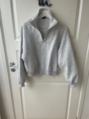 Grå halvzip sweatshirt Gina Tricot - Mysig ljusgrå sweatshirt från Gina Tricot med halv dragkedja och hög krage. Tröjan har ribbade muddar vid ärmslut och nederkant, samt en relaxed passform. Perfekt för en chill och stilren look.