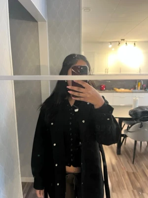 Svart overshirt med knappar - Snygg svart kappa  med knappar framtill och klassisk krage. Med ett band till. Bra skick 