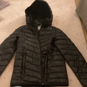 Svart dunjacka från Mckinley 🖤🖤🖤 - Svart dunjacka med quiltad design och huva. Jackan har dragkedja framtill och långa ärmar. Perfekt för kalla dagar och har en klassisk pufferstil som är både snygg och praktisk. Har lite hål (som inte märks om man inte kollar noga) och EN lös tråd som man inte heller ser. 🖤