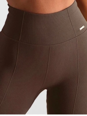 Bruna texturerade leggings Aim'n - Säljer ett par bruna leggings från Aim'n med hög midja och snygg textur i materialet. De har en tight passform och en liten metallogo framtill i midjan. Perfekta för dig som vill ha både stil och komfort.