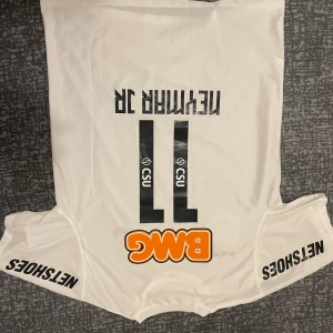 Vit Santos Neymar Jr Nike fotbollströja - Santos FC matchtröja med Neymar Jr 11 på ryggen. Vit med svarta och orange tryck, klubbmärke, sponsorer och Nike-logga. Tillverkad i lätt Dri-FIT material som andas. Klassisk rund hals och korta ärmar, perfekt för fotbollsfans.