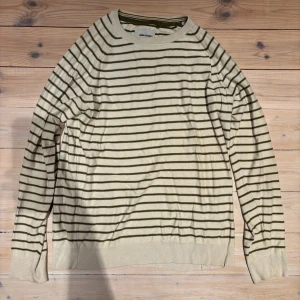 Randig beige tröja från Blend XL - Snygg beige tröja från Blend i storlek XL med olivgröna horisontella ränder. Rund halsringning med ribbad kant och diskreta färgdetaljer på insidan. Långärmad och tillverkad i mjuk bomull som känns skön mot huden. Perfekt för dig som gillar enkel och stilren design.