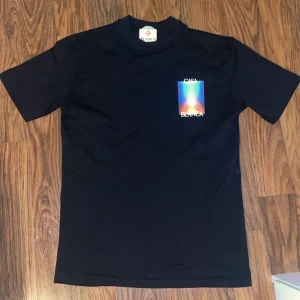 Svart t-shirt från Casablanca - Svart t-shirt från Casablanca med färgstarkt grafiskt tryck och logga på bröstet och ryggen. Klassisk passform och rund hals. Perfekt statement-plagg för dig som gillar unika prints och streetwear-vibe.