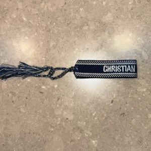 Christian Dior J'Adior blå armband - Snyggt blått armband från Christian Dior med texten 'CHRISTIAN DIOR J'ADIOR' broderad i vitt. Armbandet är gjort i tyg med flätade detaljer och fransar i ändarna. Perfekt accessoar för dig som gillar lyxiga märken och vill sticka ut. Pris går såklart att diskuteras, ställ frågor om ni har några:)