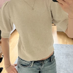 Beige stickad tröja med puffärm - Säljer en beige stickad tröja med korta puffärmar och ribbad kant vid hals, ärmslut och nederkant. 