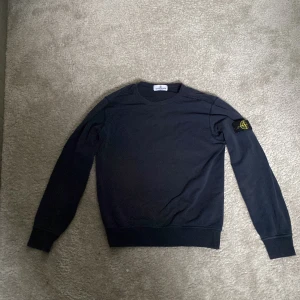 Mörkblå Stone Island sweatshirt - Snygg mörkblå sweatshirt från Stone Island Junior med klassisk rund hals och ikonisk patch på vänster ärm. Tröjan har ribbade muddar och är tillverkad i mjuk bomull som är skön att bära. Perfekt för dig som gillar streetwear och vill ha en clean look.