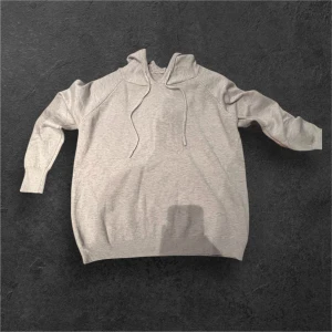 Ljusgrå hoodie med huva och snörning - En stilren ljusgrå hoodie med huva och snörning framtill. Tröjan har långa ärmar och ribbade muddar vid ärmslut och nederkant. Perfekt för chill dagar och enkel att matcha med jeans eller joggers.