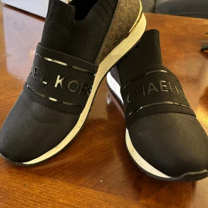 Svarta slip-on sneakers Michael Kors - Snygga svarta slip-on sneakers från Michael Kors med tydlig logga.. köp i USA .