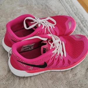 Nike rosa sneakers med vit sula - Snygga och sportiga Nike sneakers i stark rosa färg med svart swoosh på sidan. Skorna har vit platt sula och vita snören, samt mesh- och syntetdetaljer för extra ventilation. Perfekta för träning eller att lyfta din streetstyle. Lätta och flexibla med rund tå. Storlek 36
