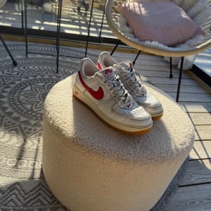 Nike Air Force 1 vit/röd sneakers - Ett par klassiska Nike Air Force 1 sneakers i en tidlös färgkombination. Skorna har en vit bas med röda detaljer på sidan och baksidan. Skorna är lite använda så det finns små saker som syns på bild 3, men i helhet så är skorna väldigt fina. Storlek 43