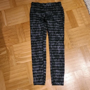 Nike Dri-Fit leggings XS svartmönstrade - Nike Dri-Fit leggings i storlek XS med svart och grått abstrakt mönster. Tight passform och stretchigt material som andas, perfekt för träning. Snygga detaljer med små knappar vid bensluten. Supersköna och stilrena tights för dig som gillar att sticka ut.