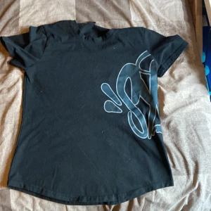 Svart t-shirt med stor grafisk print - Svart t-shirt från 0% Fucseries i storlek M. T-shirten har en stor, cool grafisk print i grått som går över både fram- och baksidan. Klassisk rund hals och korta ärmar. Skön passform och tillverkad i mjuk bomull.