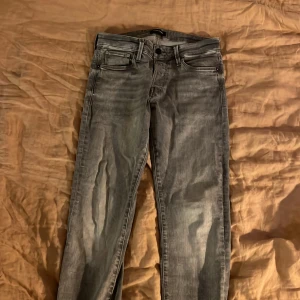 Grå slim jeans Jack & Jones 29/30 - Snygga grå jeans från Jack & Jones i modellen Slim Glenn. Jeansen har en slim passform, klassisk femficksdesign och är tillverkade i bomull. Perfekta för dig som gillar en smalare siluett och en lite tvättad look.