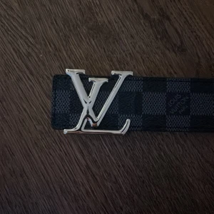 Rutigt bälte  - Rutigt bälte med silvrig text. 102 cm