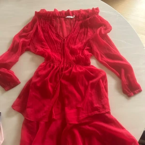 Röd omlottklänning från NA-KD XS - Snygg röd kortklänning från NA-KD i tunn, luftig polyester. Klänningen har omlottdesign, v-ringning med snörning, offshoulder och långa ärmar. Perfekt för dig som vill sticka ut med en färgstark look , använd en gång, XS men kan säga att passar även S.