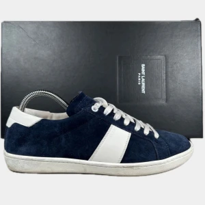 Saint Laurent blå - Snygga sneakers från Saint Laurent i marinblå mocka med vita detaljer och snörning. Klassisk låg modell med rund tå och platt sula. Vit panel på sidan och vit häl ger en stilren kontrast. Perfekta för dig som gillar exklusiva och stilrena sneakers.
