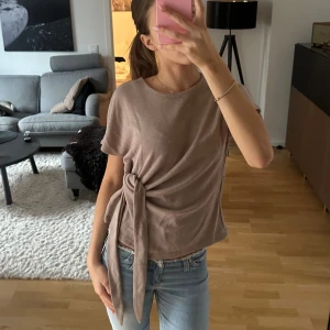 Beige omlottopp med knyt i sidan - Säljer en beige topp med knyt i sidan. Toppen har rund halsringning och korta ärmar. Super snygg till hösten och vintern😍