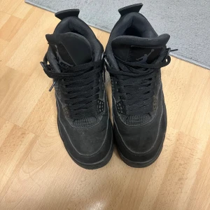 Svarta Nike Jordan 4 sneakers - Perfekt för dig som gillar streetwear och vill sticka ut. Storlek 42 eller 42,5, osäker då lappen innanför är sliten, använt skorna i drygt ett år och hänvisar till bilderna för att bedöma skicket. Sulan är sliten inuti skon så rekomenderar nya, 