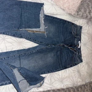 Blå wide jeans från Zara med rå kant - Säljer ett par blå jeans från Zara i storlek 34 med rak passform ner till benen och rå, fransig kant längst ner. Modellen är högmidjad och har klassiska fem fickor samt dragkedja och knapp framtill. Perfekt för dig som gillar en chill och trendig look.